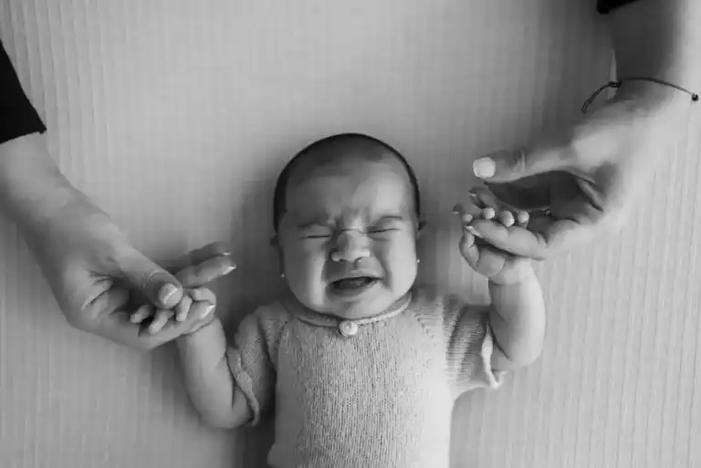 Foto en blanco y negro de un bebé recién nacido llorando intensamente con la boca abierta y las manos levantadas, en un momento de desamparo.